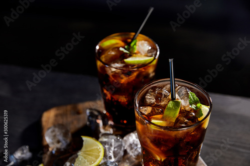 cocktails cuba libre in glasses with straws, ice cubes and limes on black background photo