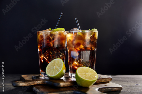 cocktails cuba libre in glasses with straws and limes on black background photo