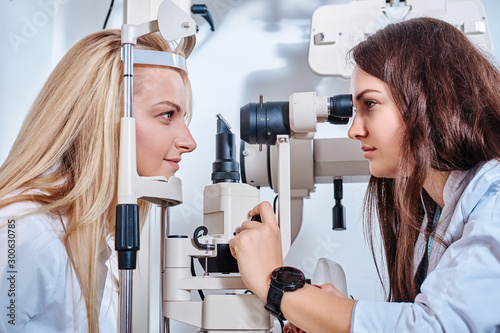 Optometrist is checking vision of young beautiful woman using special machine.