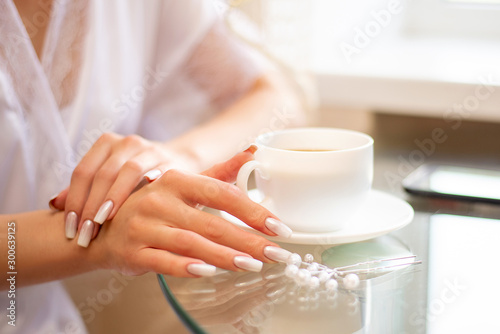 girl hand holding a white cup with coffee on a glass table in the morning by the window