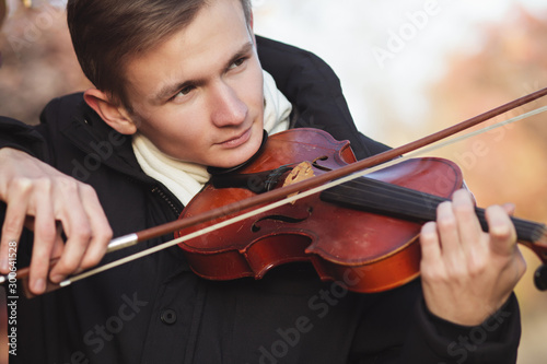 face profile of a young elegant man playing the violin on autumn nature backgroung, a boy with a bowed orchestra instrument makes a concert, concept of classical music, hobby and art