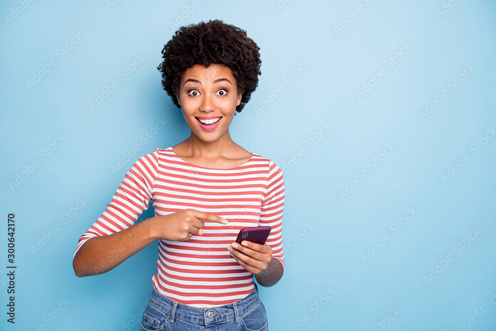 Photo of pretty dark skin lady holding telephone hands indicating finger new cool phone case wear casual striped sweater jeans isolated blue color background Photo of pretty dark skin lady holding telephone hands indicating finger new cool phone case wear casual striped sweater jeans isolated blue color background