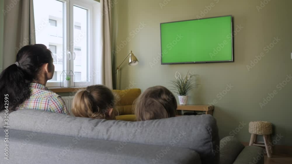 Family Sitting Together Sofa In Their Living Room Watching TV Green Screen. Rear View Of Family With Children Sitting On Sofa In Living Room Day Watching Green Mock-up Screen TV Together. Family Sitting Together Sofa In Their Living Room Watching TV Green Screen. Rear View Of Family With Children Sitting On Sofa In Living Room Day Watching Green Mock-up Screen TV Together.