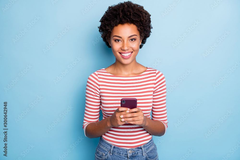 Photo of pretty dark skin lady holding telephone hands reading new post comments likes reposts wear casual striped sweater jeans isolated blue color background Photo of pretty dark skin lady holding telephone hands reading new post comments likes reposts wear casual striped sweater jeans isolated blue color background