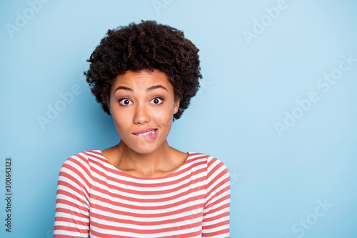 Oops. Closeup photo of pretty dark skin lady biting lips speechless made great mistake feel guilty wear striped shirt isolated blue color background