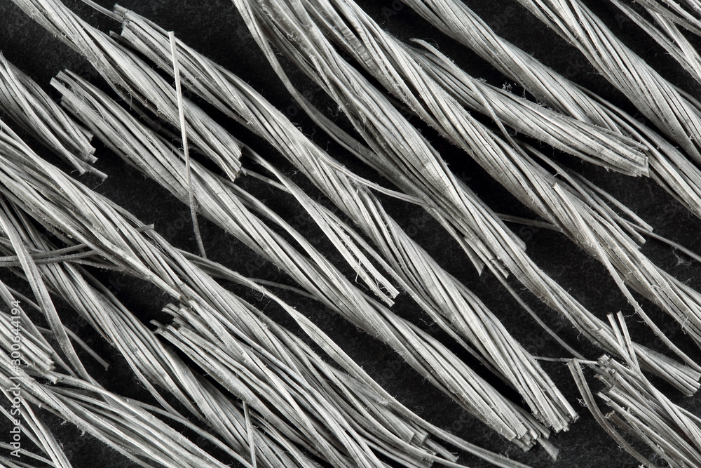 Fototapeta premium Extreme close up, top down view of bundels of grey colored, twisted polypropylene macro fibers for concrete reinforcement on black stone background