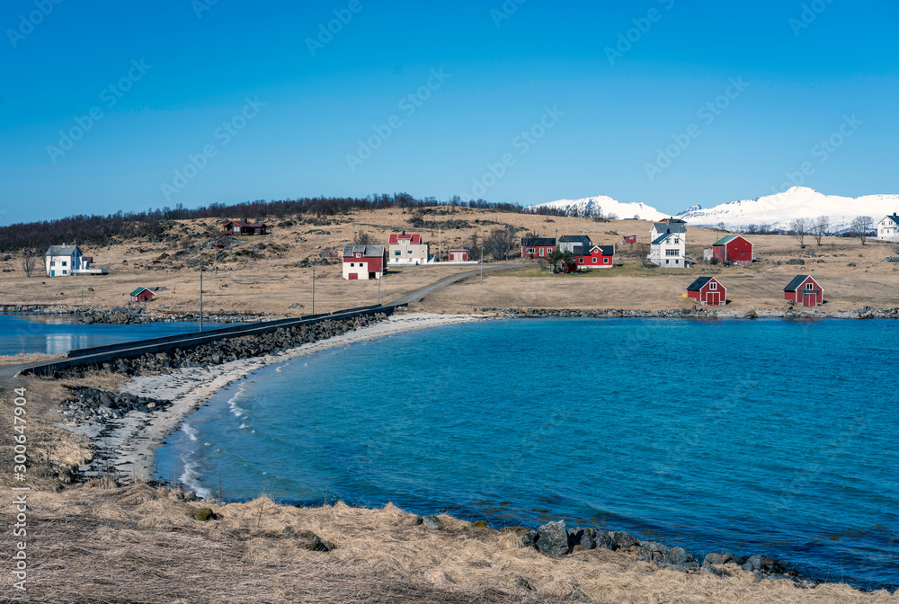Houses by the sea in northern norway in nice weather. Blue sky and snowy white peaks in the background. Travel, arctic, cold, building, lifestyle concept.