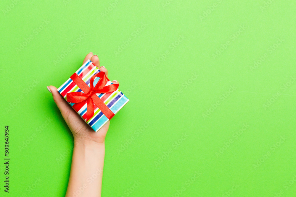 Fototapeta premium Top view of female hands holding christmas or other holiday handmade present box package in the palms, flat lay table background with copy space
