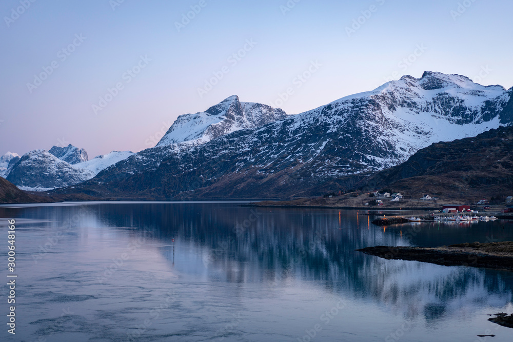 Lofoten island at night, with snowy peaks in the back and fishing village with city lights in the front. Travel and lifestyle concept.