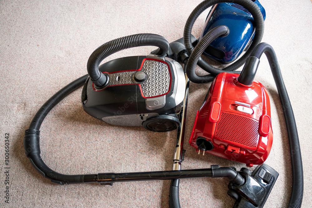 Three vacuum cleaners in different colors sitting on a white carpet floor. Equipment, household and vacuum concept.