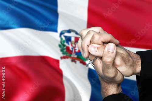 Obraz na płótnie Dominican Republic flag and praying patriot man with crossed hands. Holding cross, hoping and wishing. w salonie