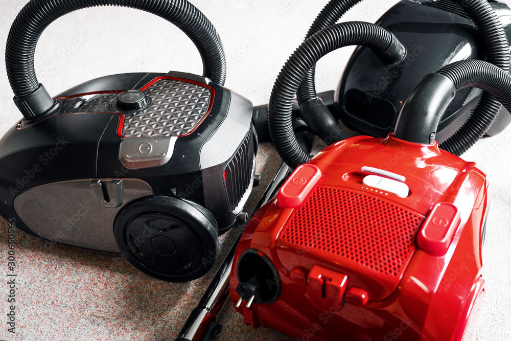Three vacuum cleaners in different colors sitting on a white carpet floor. Equipment, household and vacuum concept. Three vacuum cleaners in different colors sitting on a white carpet floor. Equipment, household and vacuum concept.