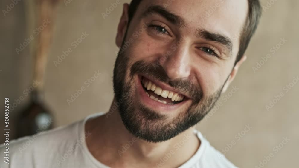 Close up view of beautiful cheerful young brunet man smiling and laughing while looking at the camera at home