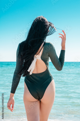 Girl with black hair is walking along the beach in a bodysuit