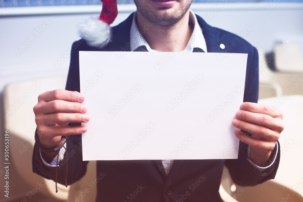 Young businessman in Santa Claus hat holding blank page. Young businessman in Santa Claus hat holding blank page.