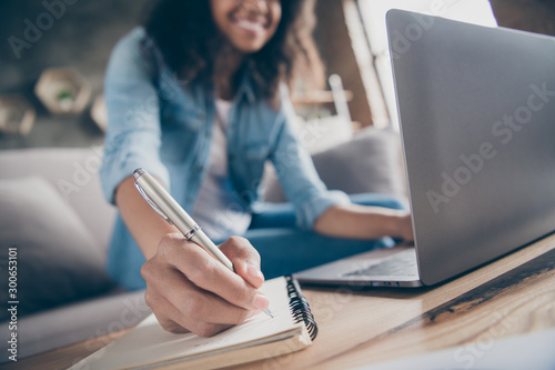 Cropped blurry focus photo of amazing dark skin curly lady browsing notebook writing pen plan list diary sitting cozy sofa wear casual denim outfit flat indoors photo