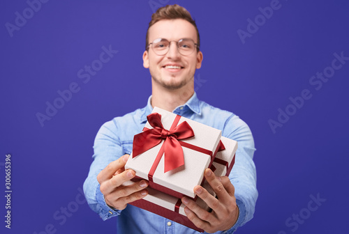 Cheerful guy in blue denim shirt and round glasses giving you gift © Svitlana