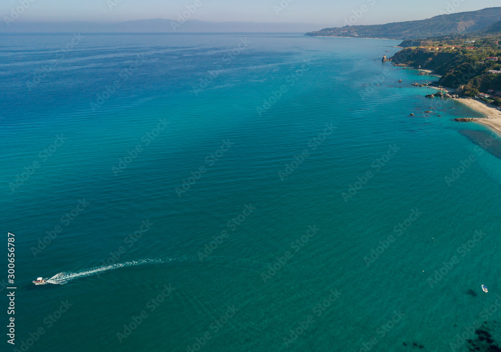 Aerial view of a motor boat sailing near the rocks and the beach of Tropea, Calabria, Italy