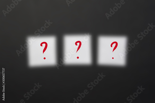 Ready-made inscription with three question marks on white squares of paper on a dark blurred background.