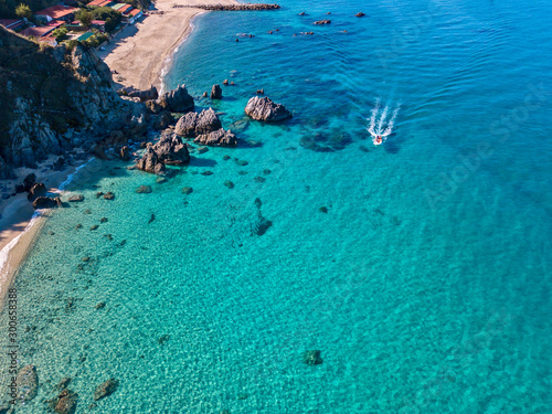 Aerial view of a motor boat sailing near the rocks and the beach of Tropea, Calabria, Italy