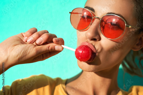 Canvas Print Close up portrait of a young stylish woman sexually licking a big red lollipop against blue background