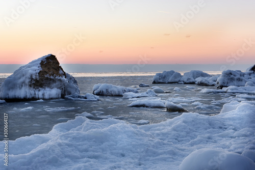 Frosty winter dawn on the seashore. The shore and stones covered with snow and ice.