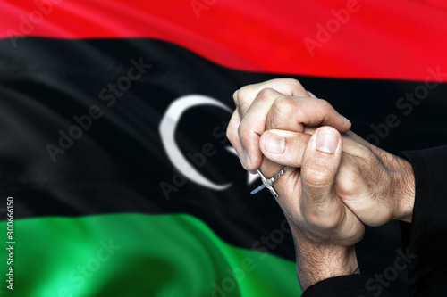 Libya flag and praying patriot man with crossed hands. Holding cross, hoping and wishing.