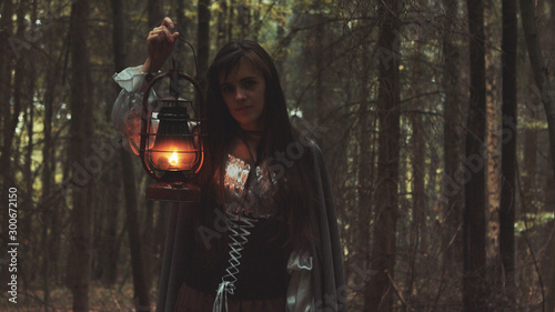 Young girl with a lantern wandering old forest. Gothic scene from the movie.