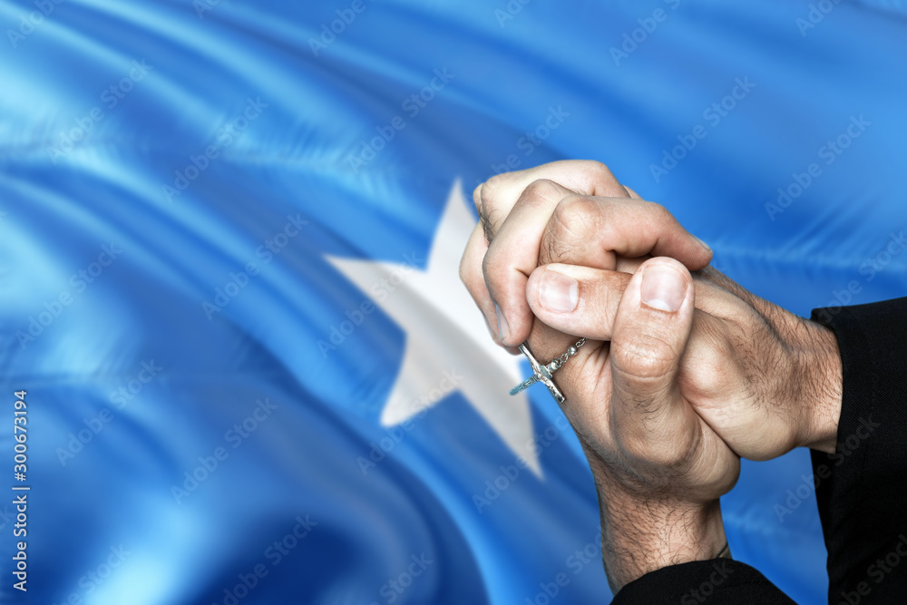 Somalia flag and praying patriot man with crossed hands. Holding cross, hoping and wishing.