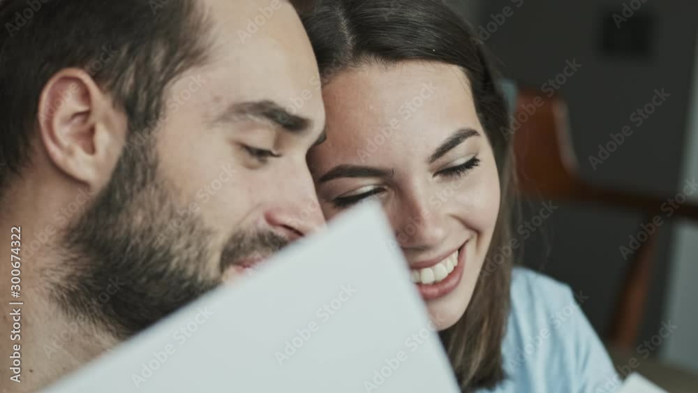 Cropped view of cheerful young lovely couple looking at family pictures and smiling while sitting at home Cropped view of cheerful young lovely couple looking at family pictures and smiling while sitting at home