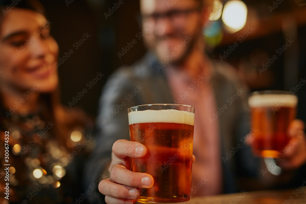 Man standing in group and giving beer to a friend. Irish pub interior. Nightlife.
