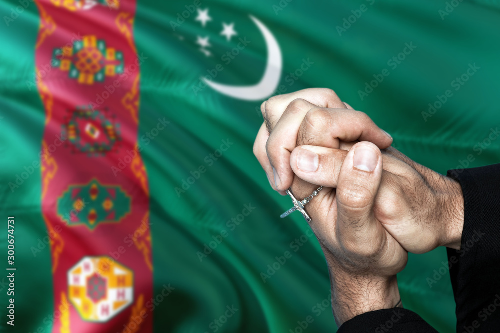 Turkmenistan flag and praying patriot man with crossed hands. Holding cross, hoping and wishing.