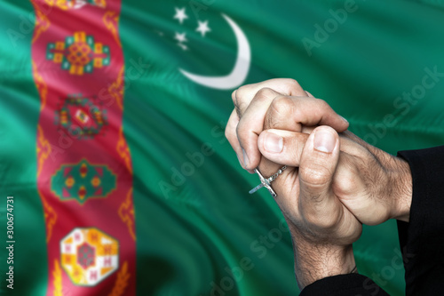 Turkmenistan flag and praying patriot man with crossed hands. Holding cross, hoping and wishing.