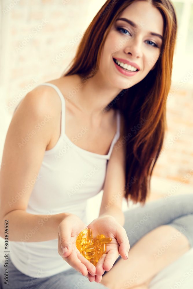 Portrait of smiling young lovely girl with Omega 3 fish oil capsule, at home. Health care and medical concept with caucasian beautiful model.