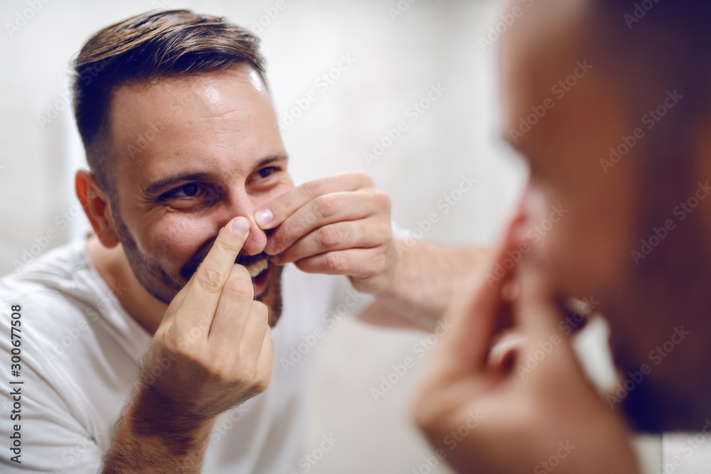 Close up of handsome caucasian man looking himself in the mirror and squeezing blackhead on his nose. Close up of handsome caucasian man looking himself in the mirror and squeezing blackhead on his nose.