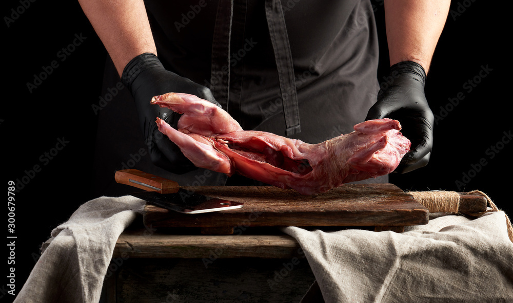 chef in black latex gloves holds a whole rabbit carcass