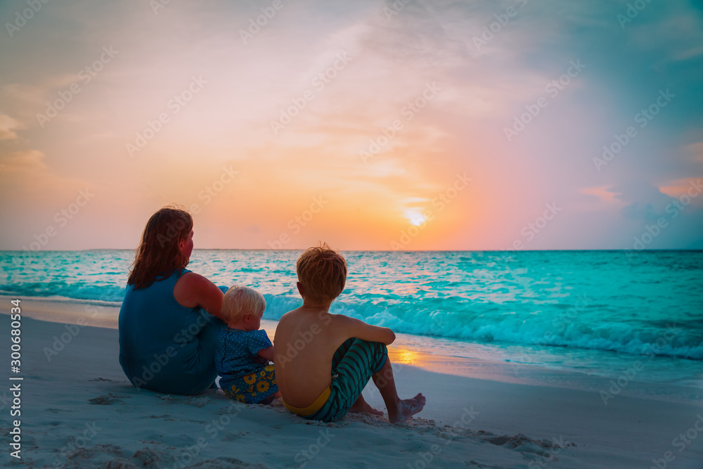 mother with son and daughter looking at sunset on beach