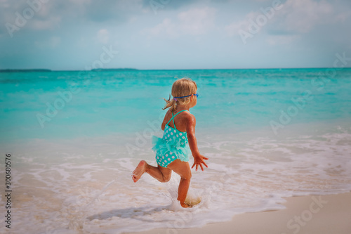 happy little girl run and play with waves on tropical beach