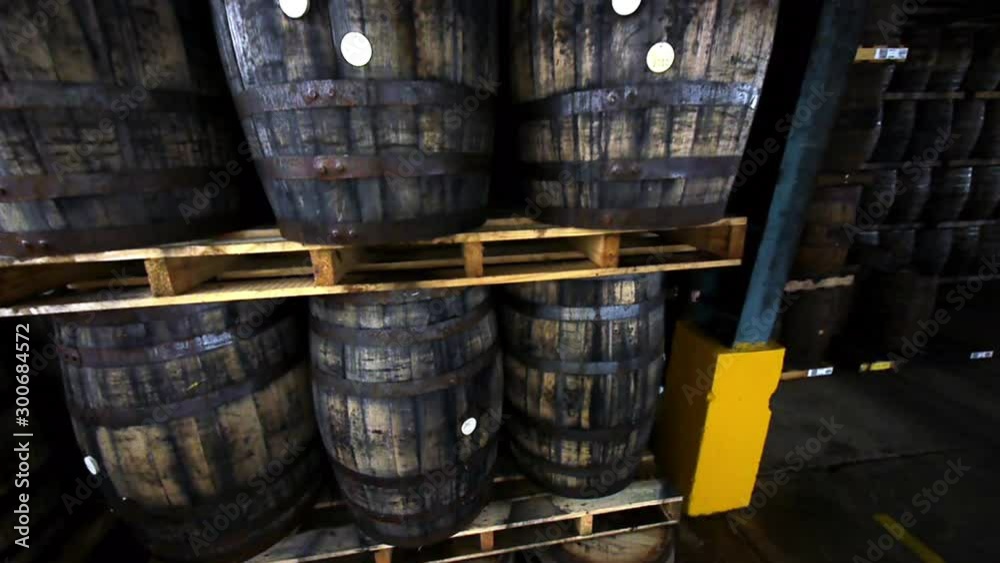 Pedestal up the side of wooden barrels stacked on pallets and tilting down to show a warehouse filled with whiskey barrels Pedestal up the side of wooden barrels stacked on pallets and tilting down to show a warehouse filled with whiskey barrels