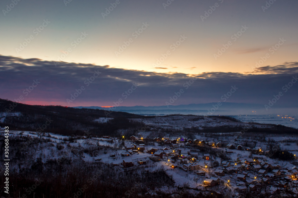 Winter scenery, village in valley with lights shining through the windows.