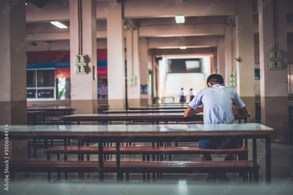 Male high school student is sitting alone in the school cafeteria, Thailand, southeast Asia. - obrazy, fototapety, plakaty 