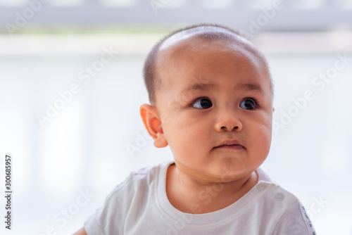 A cute Asian male baby wearing a white shirt  about six months old is smiling on a white background.