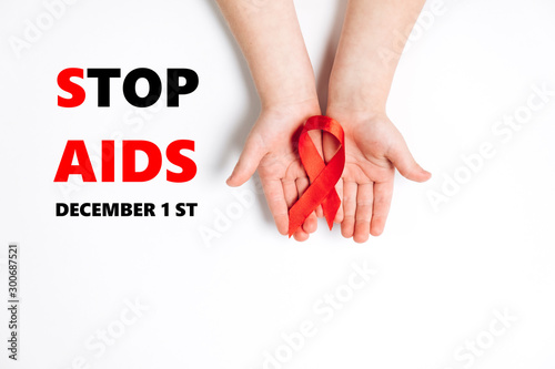 Top view on child's hands holding red ribbon on white background, HIV awareness concept, world AIDS day. Flat lay, copy space