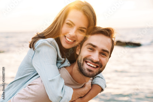 Image of young happy man giving piggyback ride beautiful woman