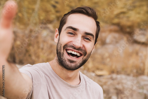 Image of unshaven caucasian man laughing and taking selfie photo