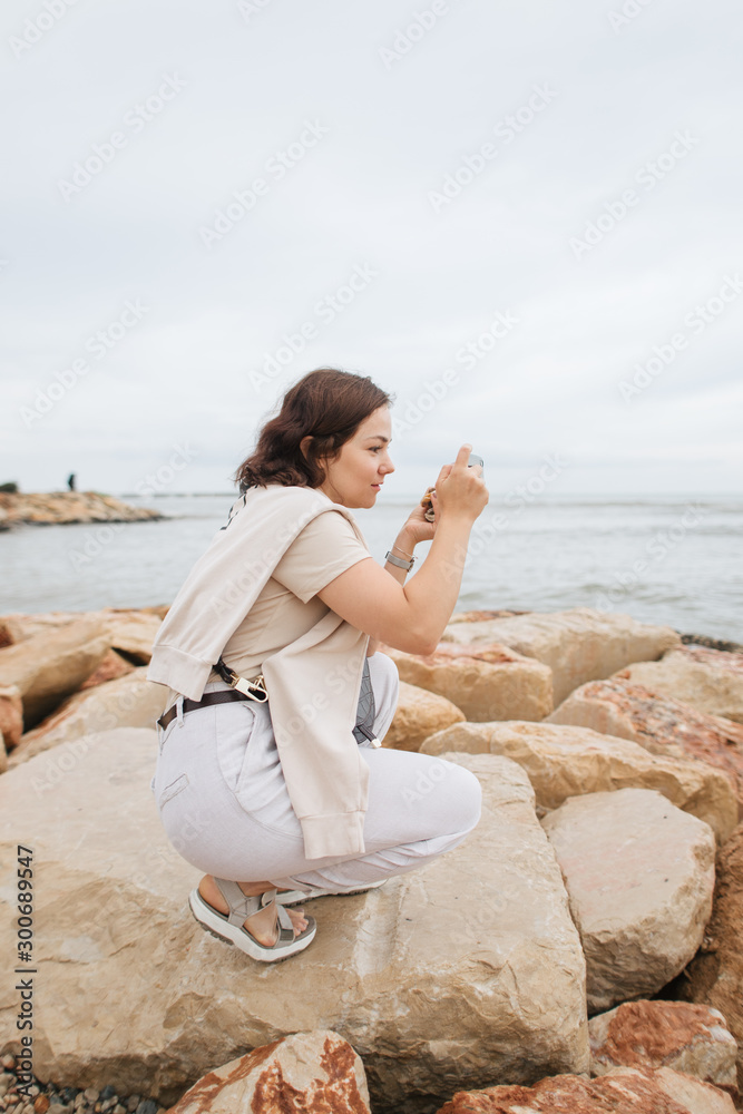 woman makes photo on smartphone on stones near sea