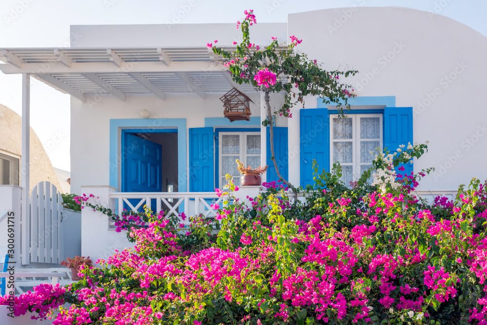 Building in Santorini with blue details and purple flowers in the garden. Travel, house, building, sunny, summer, culture concept.