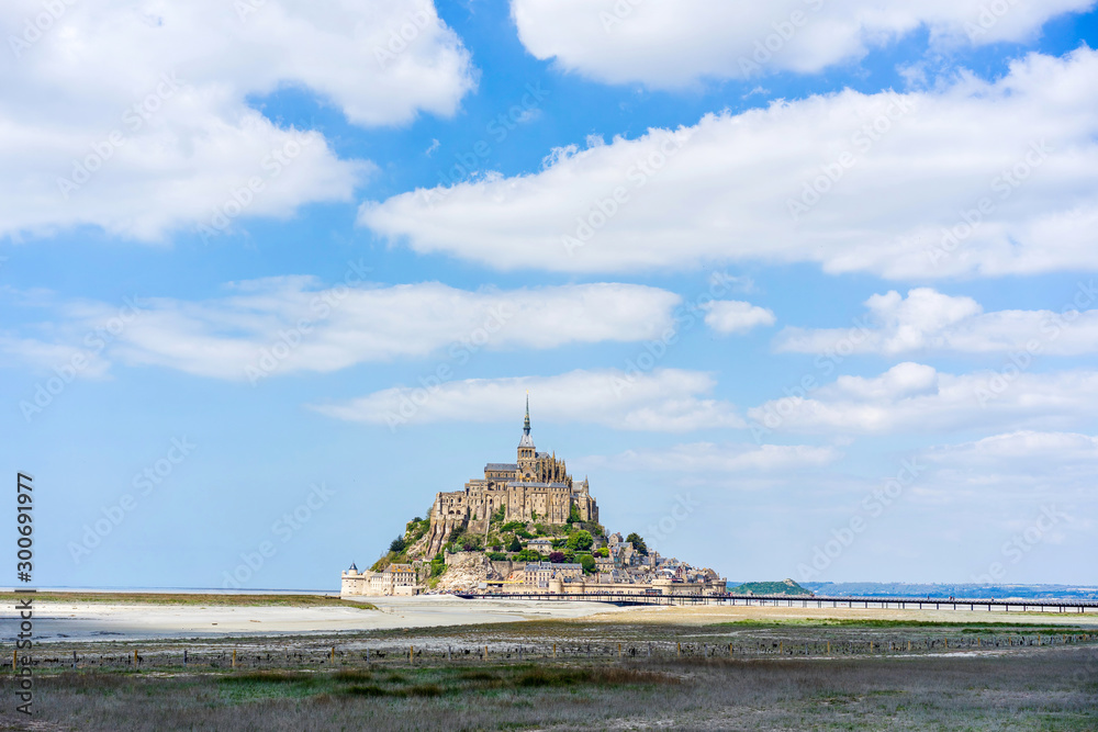 Distant view of Mont Saint Michel in low tide west France with clouds in the blue sky