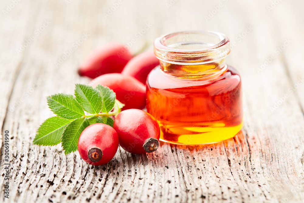 Rose hips oil with berries on wooden background - obrazy, fototapety, plakaty 