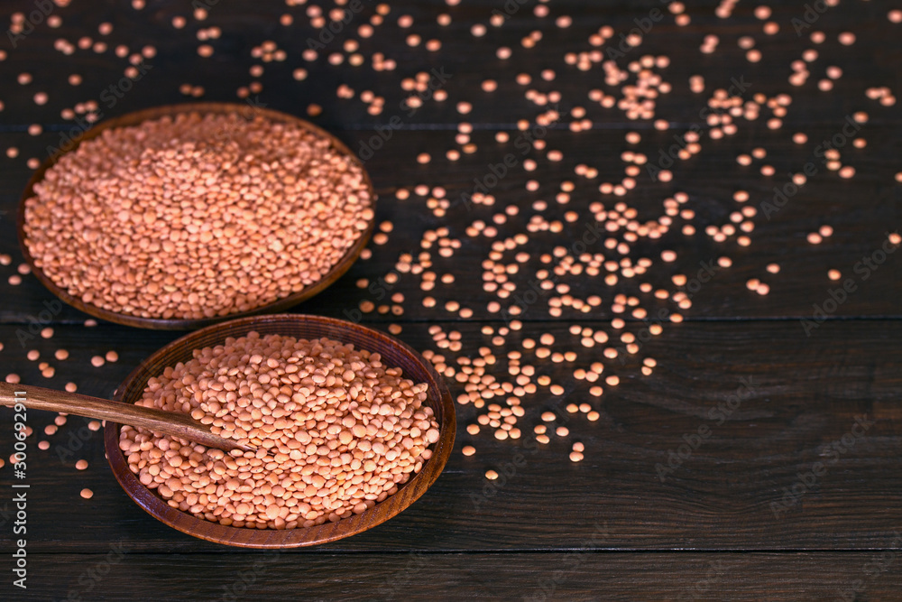 red raw lentils in wooden bowls and scattered on a wooden table close-up. background with lentils. red raw lentils in wooden bowls and scattered on a wooden table close-up. background with lentils.